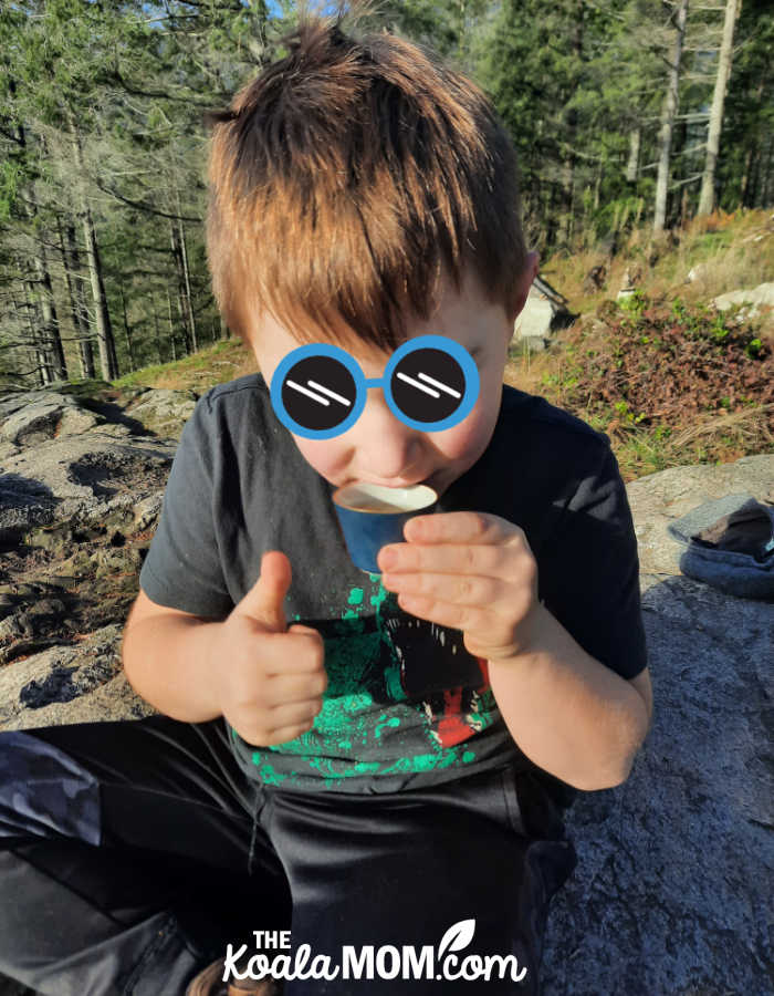 Boy drinks tea outdoors while giving a thumbs up. Photo by Bonnie Way.